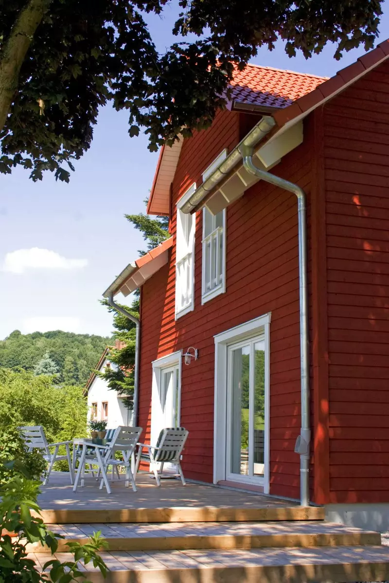Ein rotes Haus mit weißem Zaun und grünem Garten.