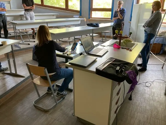 Eine Gruppe von Personen sitzt in einem Klassenzimmer mit Laptops vor sich.